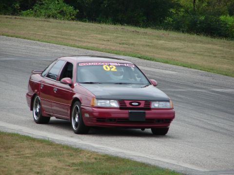 1993 Ford Taurus - A red 1993 Ford Taurus SHO competes on a road course, displaying the number 02 on its windshield.