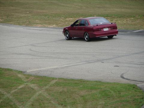 1993 Ford Taurus - A red sedan with a spoiler is seen on a track, leaving tire marks.