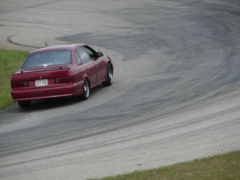 1993 Ford Taurus - A red 1993 Ford Taurus navigates a turn on a race track, leaving tire marks on the asphalt.