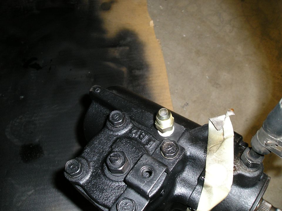 Close-up of a black steering gear box with bolts and a brass fitting