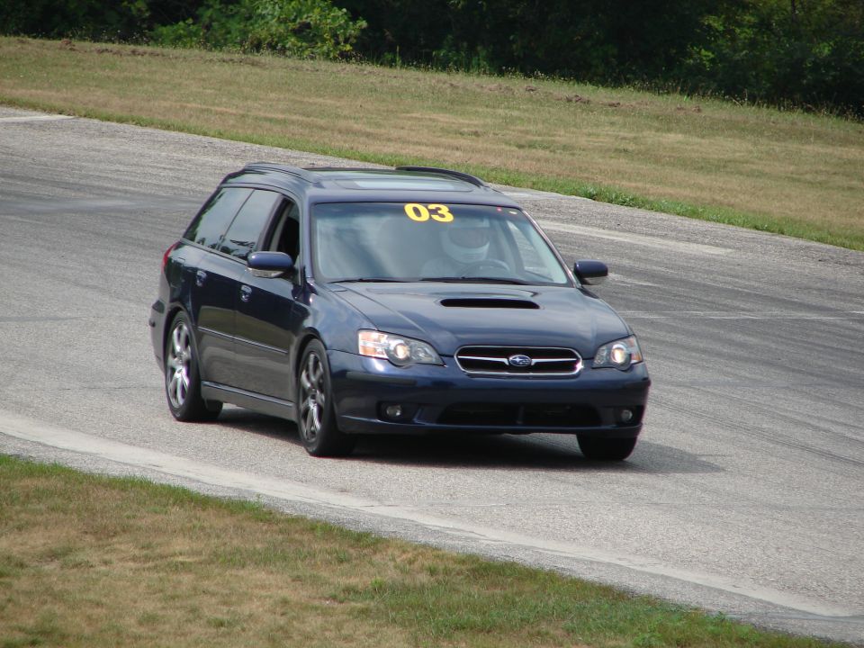 dark blue Subaru Outback wagon with yellow 03 on windshield driving on a race track
