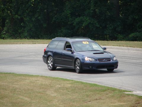 1993 Ford Taurus - A dark blue Subaru Outback wagon navigates a turn on a race track, displaying the number '03' on its windshield.