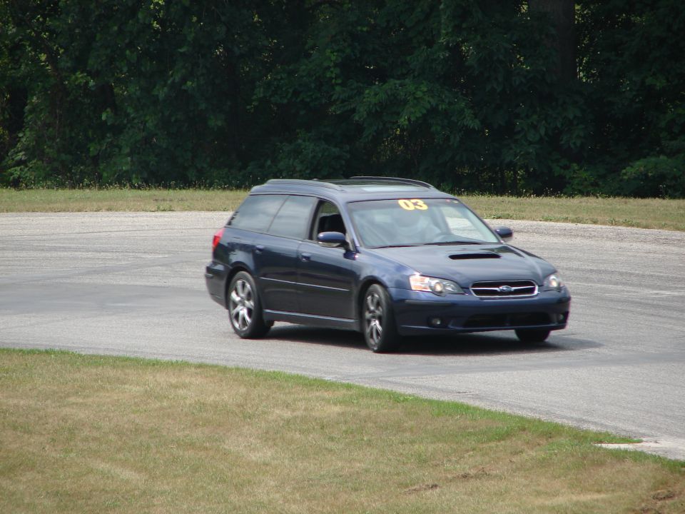Dark blue Subaru Outback wagon with yellow '03' sticker on windshield, on race track