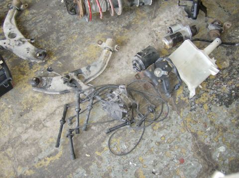 1996 Ford Probe - Various automotive parts, such as control arms and spark plug wires, are scattered across a worn concrete surface.