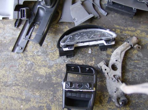 1996 Ford Probe - Various car parts including a dashboard cluster and suspension arm are scattered on a rough surface.