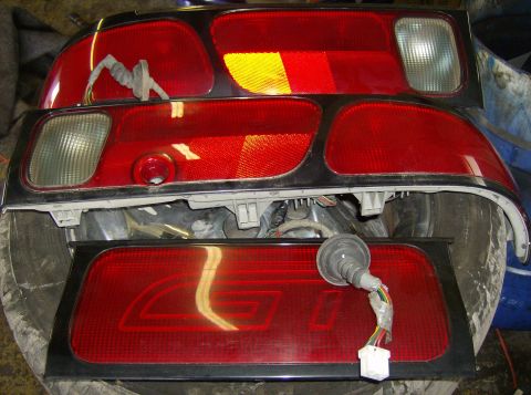 1996 Ford Probe - Several red taillight assemblies are stacked, with one a prominent "GT" emblem and wiring harness.