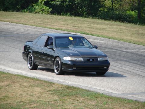 1993 Ford Taurus - A black 1993 Ford Taurus with racing number 6 on the windshield navigates a turn on a road course.