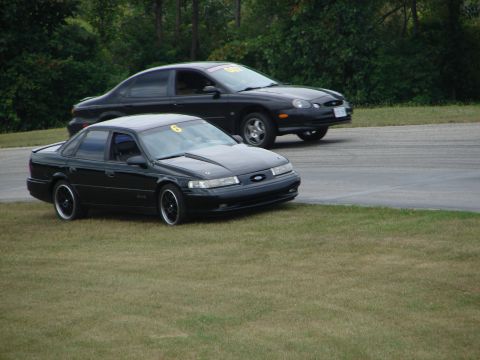 1993 Ford Taurus - Two black sedans are on a race track, with one car in the foreground and another in the background.