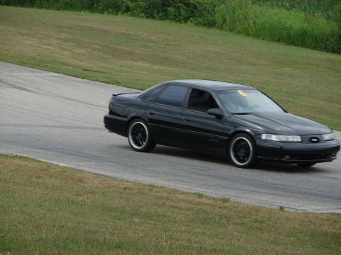 1993 Ford Taurus - A black 1993 Ford Taurus navigates a turn on a road course, displaying the number 6 on its windshield.