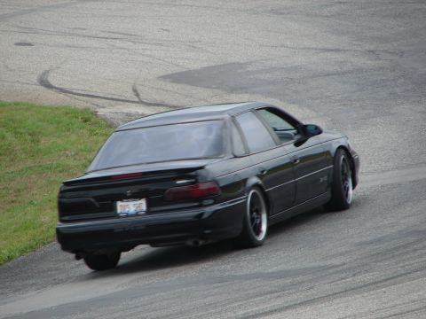 1993 Ford Taurus - A black 1993 Ford Taurus is seen on a race track, with tire marks visible on the asphalt.
