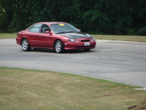 1993 Ford Taurus - A red sedan with a contrasting black hood navigates a turn on a paved track, marked with the number 08.