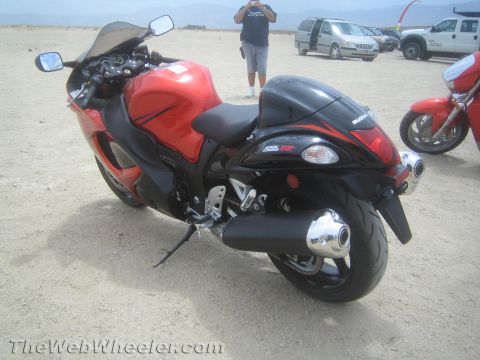 1990 Ford Bronco - Rear three-quarter view of a red and black Suzuki Hayabusa sportbike parked on desert ground, with a person and vehicles in the background.