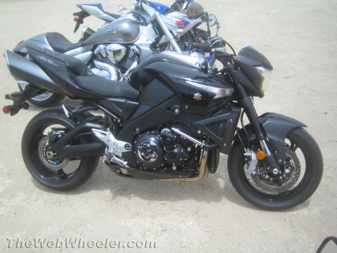 1990 Ford Bronco - Left-side profile of a black Suzuki naked motorcycle parked on dirt, with a silver cruiser and blue sportbike lined up behind.