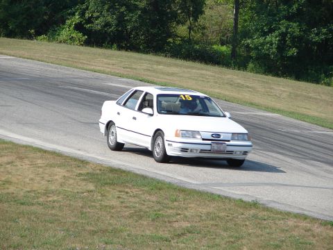 1993 Ford Taurus - A white 1993 Ford Taurus is seen on a road course, displaying the number 15 on its windshield.
