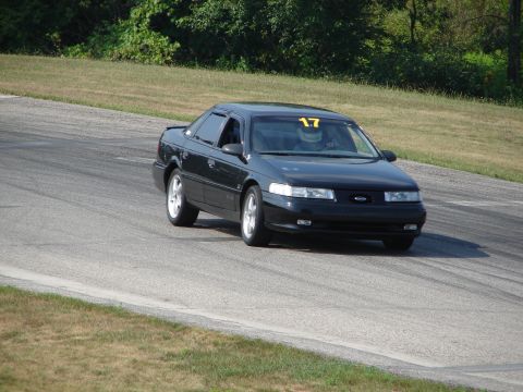 1993 Ford Taurus - A black 1993 Ford Taurus is on a racetrack, driven by a person in racing gear.