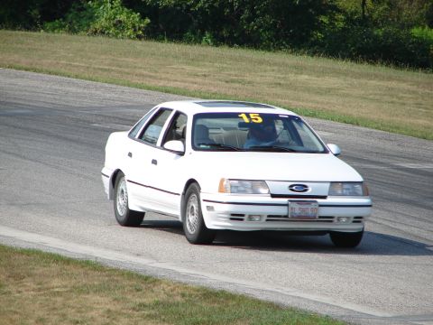 1993 Ford Taurus - A white 1993 Ford Taurus sedan navigates a turn on a road course, displaying racing number 15.