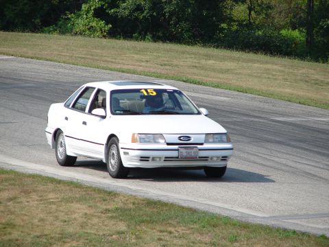 1993 Ford Taurus - A white 1993 Ford Taurus with racing number 15 visible on the roof drives on a road course.