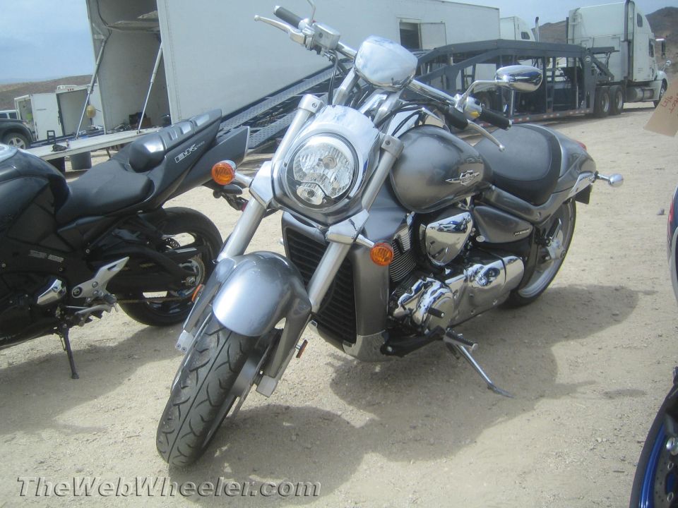Silver Suzuki cruiser motorcycle front view parked by trailers and trucks