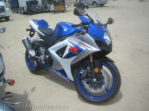 1990 Ford Bronco - blue, white and silver Suzuki GSX-R sportbike parked on a dirt lot, with shop equipment and a truck in the background.