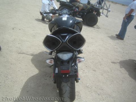 1990 Ford Bronco - Rear view of a black Suzuki sportbike showing its dual under-tail exhaust outlets and taillight, with people and an ATV behind.