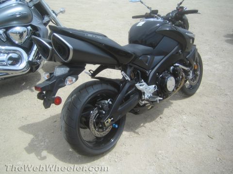1990 Ford Bronco - Rear three-quarter view of a black Suzuki naked motorcycle with a single-sided look exhaust, parked on dirt beside a silver cruiser.