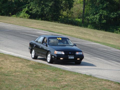 1993 Ford Taurus - Black 1993 Ford Taurus driving on a road course with a yellow number 19 on the windshield.