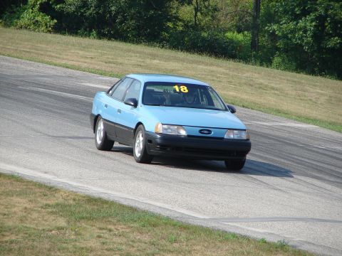 1993 Ford Taurus - A light blue sedan with a racing number on its windshield navigates a turn on a paved track.