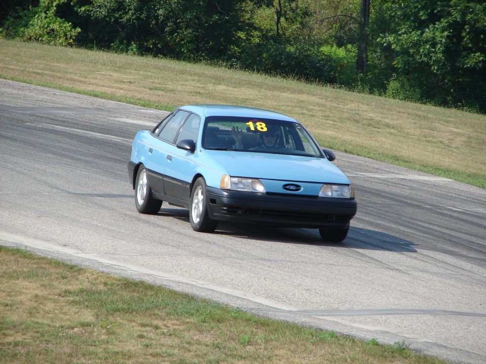 Light blue sedan with black trim and racing number 18 on windshield driving on a track