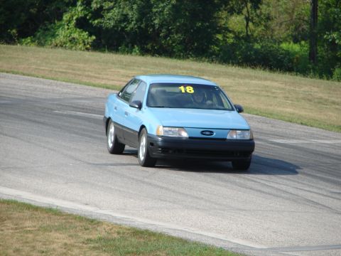 1993 Ford Taurus - A light blue sedan with racing number 18 navigates a turn on a road course.