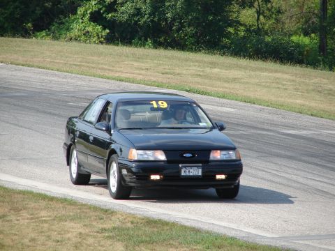 1993 Ford Taurus - A black 1993 Ford Taurus navigates a turn on a road course, displaying the number 19 on its windshield.