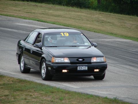 1993 Ford Taurus - A black sedan, likely a 1992 model, navigates a turn on a road course with a racing number displayed.