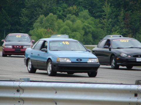 1993 Ford Taurus - Several Ford Taurus models compete on a road course, with racing numbers displayed on their windshields.