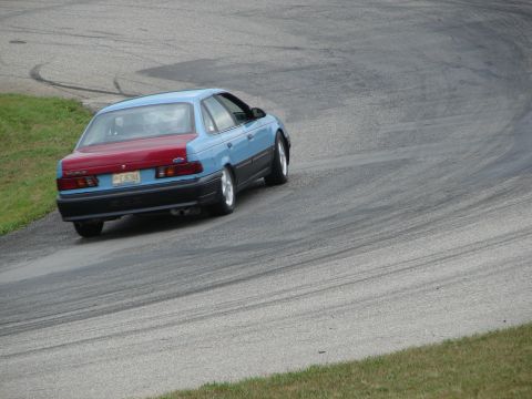 1993 Ford Taurus - A blue and red 1993 Ford Taurus navigates a turn on a road course.