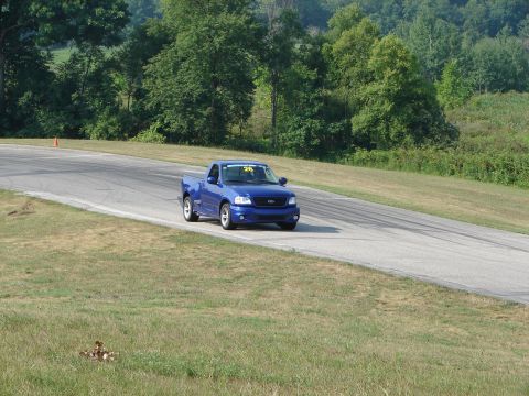 1993 Ford Taurus - Blue 2001 Ford F-150 SVT Lightning pickup truck navigates a turn on a road course.