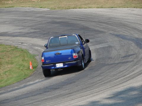 1993 Ford Taurus - A blue SVT Lightning pickup truck navigates a turn on a paved race track.