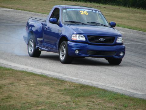 1993 Ford Taurus - A blue 1999 Ford F-150 SVT Lightning drifts on a road course, emitting smoke from its tires.