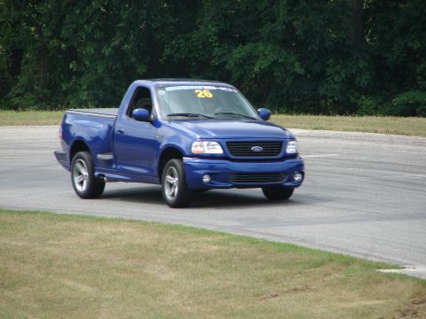 1993 Ford Taurus - A blue 1999 Ford F-150 SVT Lightning pickup truck is seen on a road course with racing decals.
