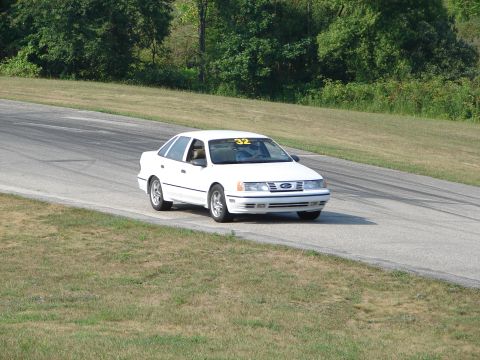 1993 Ford Taurus - A white 1993 Ford Taurus navigates a turn on a road course, displaying the number 32 on its windshield.