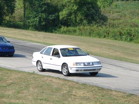1993 Ford Taurus - White 1993 Ford Taurus competes on a road course, with another vehicle visible in the background.
