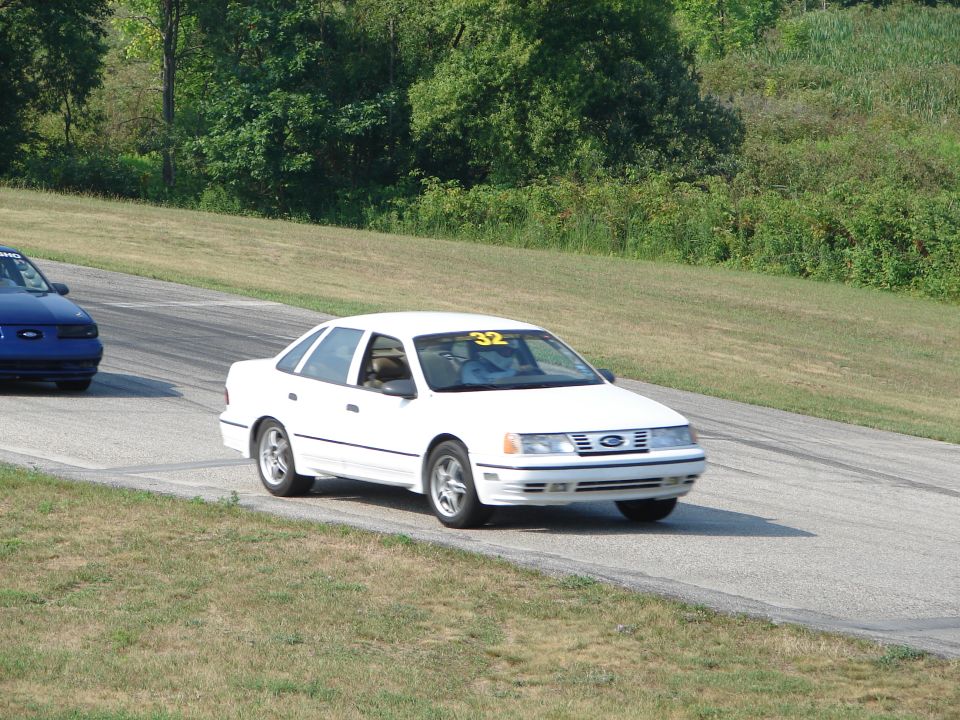 1993 Ford Taurus on a race track with a blue car behind it