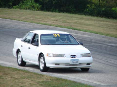 1993 Ford Taurus - A white sedan with racing number 31 navigates a turn on a paved road course.