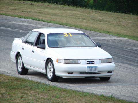 1993 Ford Taurus - A white 1993 Ford Taurus navigates a turn on a road course, displaying the number 31 on its windshield.