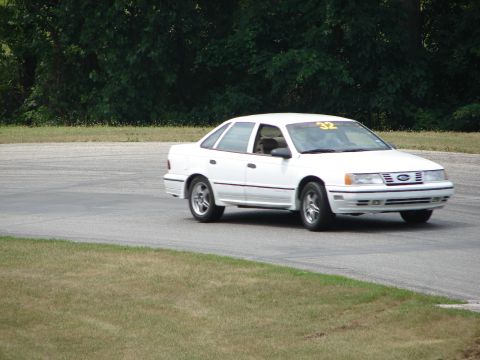 1993 Ford Taurus - A white sedan, possibly a 1992 model, navigates a turn on a road course with a racing number displayed.