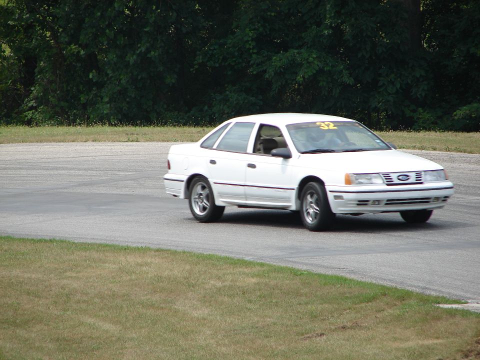 White sedan with racing number 32 on windshield, driving on a road course