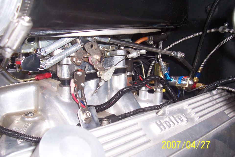 Engine close-up with carburetor linkage, springs, braided lines, and finned Holley valve cover