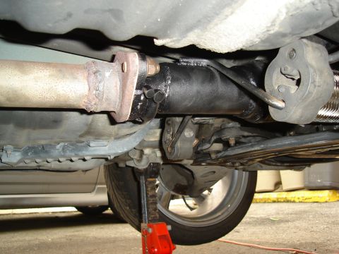 1995 Mazda MX-6 - The underside of a vehicle is shown, with a focus on the exhaust system and suspension components, supported by a jack.