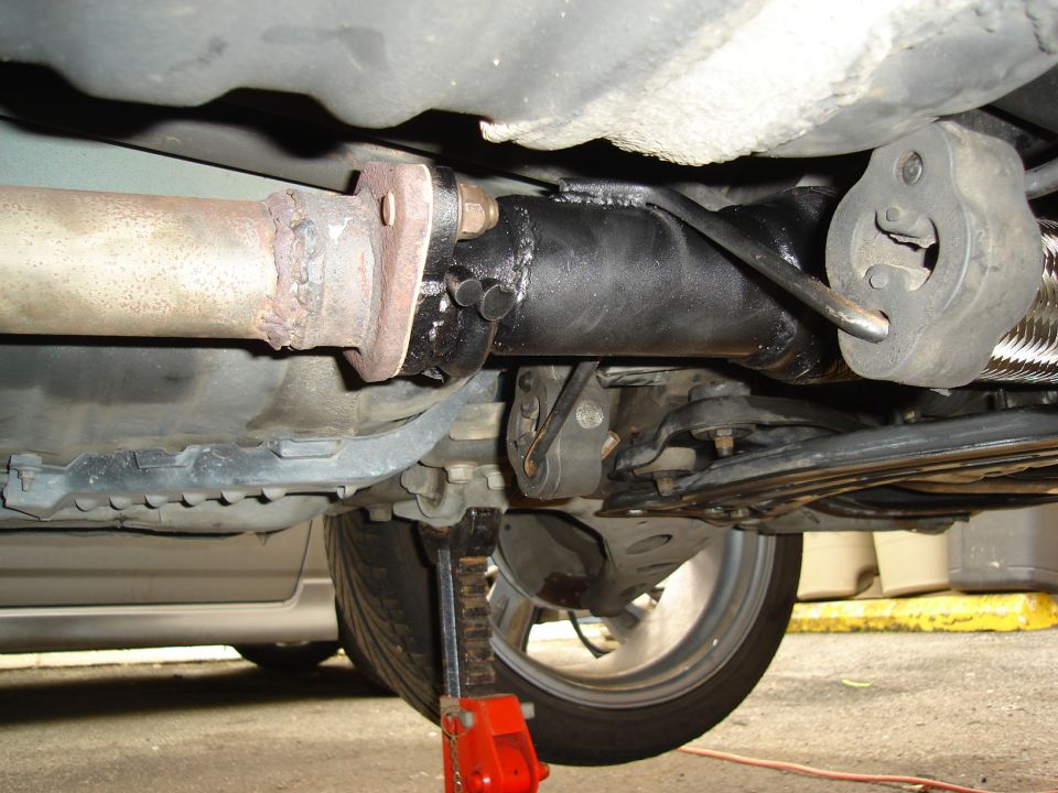 Underside of a car showing exhaust pipe, suspension, and a red jack under the wheel