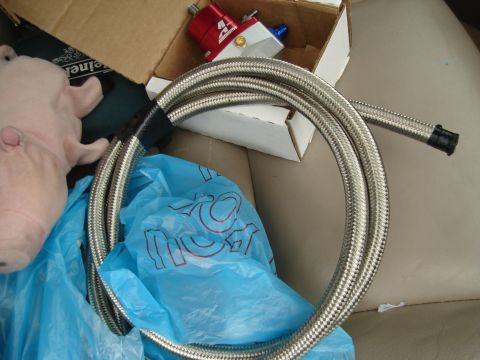 1995 Mazda MX-6 - A red fuel pressure regulator and braided hose are shown, along with a plush pig toy and a blue plastic bag.