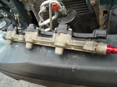 1995 Mazda MX-6 - A close-up view of a fuel rail assembly, showing its connection to various engine parts and the vehicle's radiator.