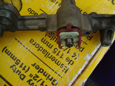 1995 Mazda MX-6 - Close-up of a fuel rail component, possibly for a turbo project, resting on a yellow surface with visible text.